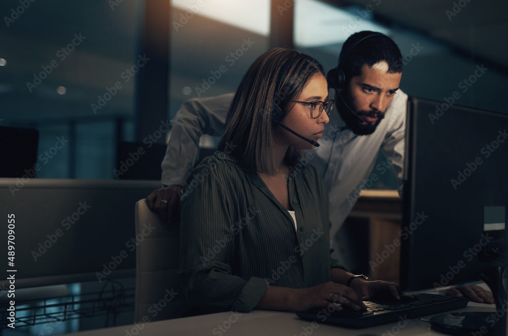 Poster together we can get it done. shot of two call centre agents working together in an office at night.