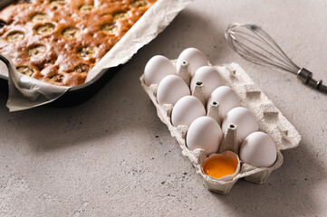 Chicken white eggs in a pan on a light background, one egg is broken and seen yolk, baked cake on the far plan, rear side light