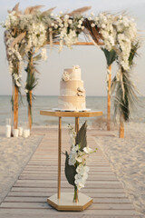 Wedding cake at a beach wedding on the background of a beautiful arch for an exit ceremony.