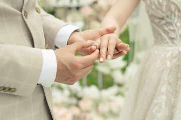 A married couple exchanges wedding rings at a wedding ceremony. The groom put the ring on the finger of his beautiful wife.