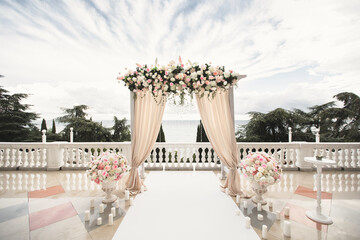 The wedding arch decorated with flowers stands in the luxurious area of the wedding ceremony.