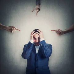 Ashamed and desperate businessman covers head with hands, as multiple persons pointing fingers towards him, blaming and scolding. Man suffering emotional breakdown and depression, being under pressure - 489711004