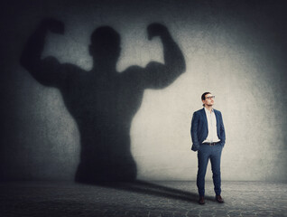 Confident businessman keeps hands in his pockets while casts a powerful person shadow on the wall...