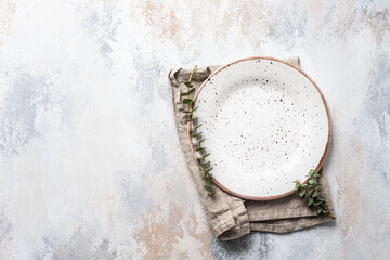 Empty plate, linen napkin and eucalyptus branches, light concrete background. Spring menu concept. Trendy minimal style tableware. Mockup menu for restaurant. Top view, copy space.