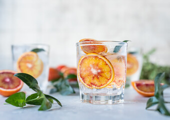 Tonic nonalcoholic mocktail with red Sicilian oranges and ice, grey background. Cold refreshing summer mojito lemonade.