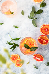 Gin and tonic alcohol drink with blood Sicilian oranges and ice on blue background. Cold refreshing cocktail.