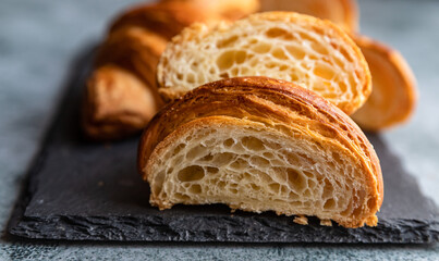 Cut in half croissant with inside texture and thin crisp layers on black board, grey background. Delicious french pastry.