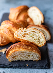Cut in half croissant with inside texture and thin crisp layers on black board, grey background. Delicious french pastry.
