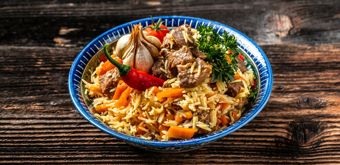 Traditional uzbek meal called pilaf. Rice with meat on plate with oriental ornament on a dark wooden background, Long banner format. space for text