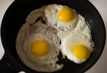 three fried eggs in a black skillet with butter