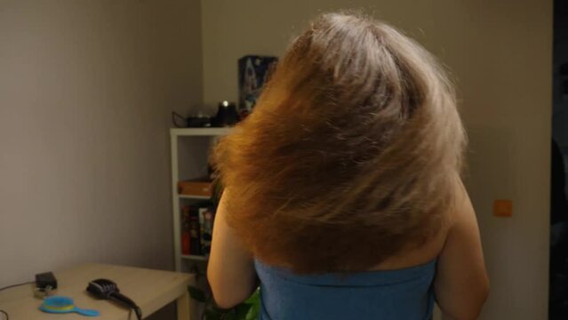 Back view of a woman shaking her long bouffant hair. The video is reversed. Slow motion