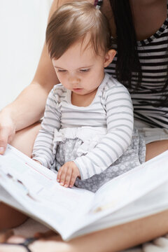 Shes already learning. Shot of a cute little baby girl sitting sitting on her moms lap looking through a picture book.