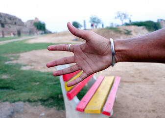 Man shows his hand hello against an empty bench at park