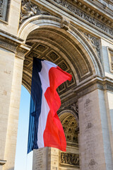 A large french flag is fluttering under the Arc de Triomphe in Paris, France.