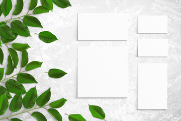 Tree branches with green leaves and white watercolor sheets of paper on a light gray concrete background. Advertising board, poster mockup for your design. Flat lay, close up, top view, copy space