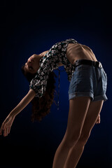 Young flexible girl posing against dark blue background. Ballet dancing pose.