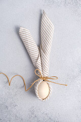Wooden Egg wrapped in linen striped napkin tied with jute in form Easter bunny with ears form on light gray background. Minimalism concept, vertical Easter card with copy space in pastel colors.