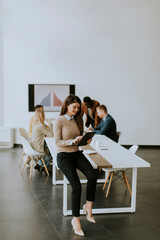 Young business woman standing in the office and using digital tablet in front of her team