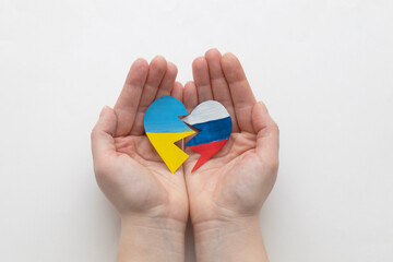 The concept of ending the war in Ukraine. Broken heart in the colors of the flag of Ukraine and Russia in female hands.