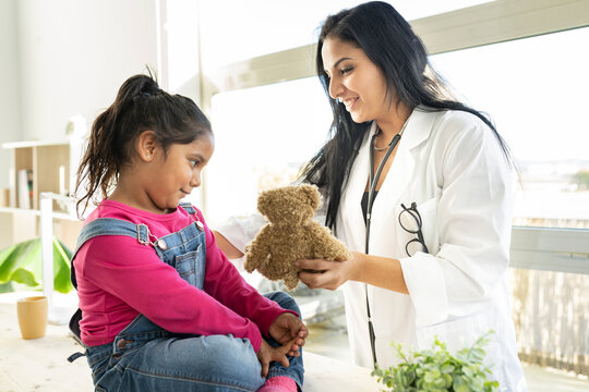 female doctor gives teddy bear to children