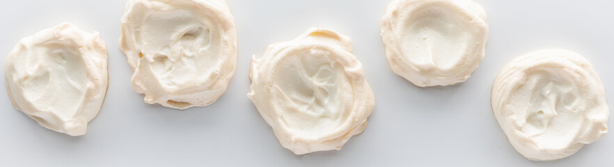 A narrow view of a row of homemade meringues against a white background.