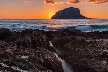Obraz premium Jagged rocks in foreground and giant rocky mountain on island at colorful sunrise, Monemvasia Greece
