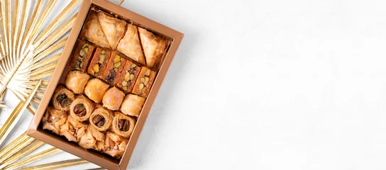 Fotobehang Web banner with collection of Eastern sweets in the golden box and copy space on white. Arabian baklava and ush-el-bul-bul dessert. Top view © kcuxen