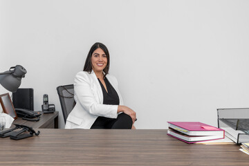 Businesswoman sitting at her desk while looking at the camera smiling. Confident female executive in her office