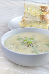 Cream of Celery Soup in a White Bowl with Blurred Egg Salad Sandwich in Background