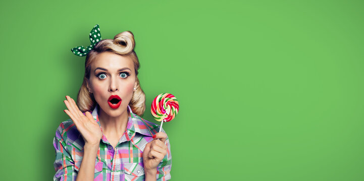 Excited surprised woman with lollipop. Girl pin up with open mouth. Blond model at retro fashion and vintage concept. Green color background. Copy space for advertise text.