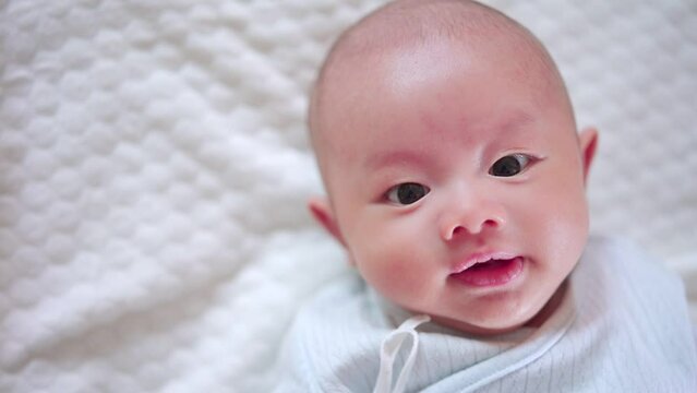 Adorable, Asian newborn lying on bed. Baby boy looking camera and laughing smile happy face. Little innocent new infant child in first day of life. Mother day concept.