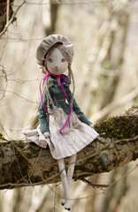 A charming beige doll cat with green eyes dressed in a jacket, dress and cap sitting on a tree.