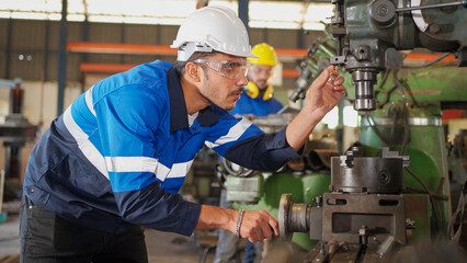 Engineer man check the operation of the equipment by turning part of machine at CNC factory. Worker wearing safety glasses and helmet. Maintenance, repairing and inspector concept.