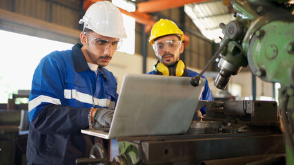 Two engineers man standing in front of equipment in CNC metal machine factory. Manager looking at tablet and see information how to fix the equipment and explain detail. Discuss and repair