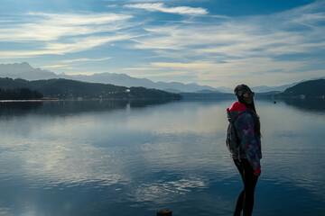 Fototapeta na wymiar Happy woman standing on the pier at beautiful Woerthersee in Poertschach, Carinthia, Austria. Scenic lake landscape surrounded by Karawanks Alps. Fresh and clean air. Reflection in Lake Woerth