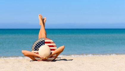 A slender girl on the beach in a straw hat in the colors of the USA flag. The concept of a perfect vacation in a resort in the United States. Focus on the hat.