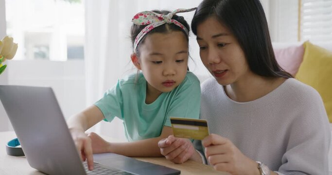 Young girl little kid help mom pay school charge tuition term fee or tax bill on web social media app relax smile at home sofa. Asia people happy playful fun buy gift card on online shop on laptop.