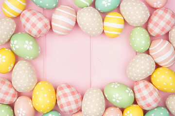 Easter frame with rustic cloth and pastel colored eggs over a pink wood background. Overhead view with copy space.