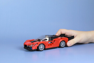 A red car from the designer in a man's hand on a blue background, space for text. The concept of insurance, purchase, sale of cars