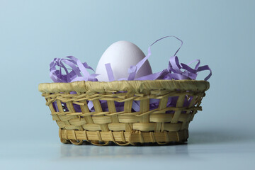 White chicken egg in a wicker basket with purple tinsel, Easter concept, close-up