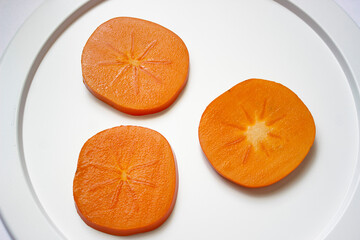 White dish with sliced juicy persimmon slices close-up