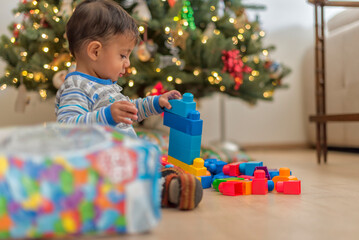 Obraz na płótnie Canvas Little latin baby boy enjoying his christmas presents by the tree