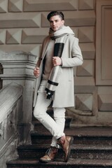 Young man wearing coat walking in the street. Young bearded guy with modern hairstyle in urban background