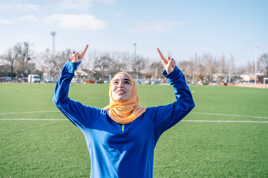 Smiling Arab female raising forefingers on sports field