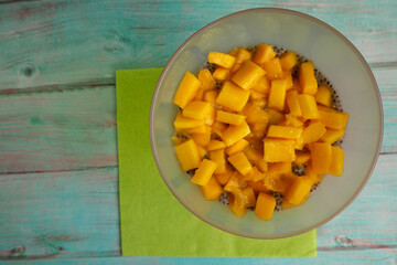 chia pudding with coconut milk and mango in a pink glass glass stands on a blue wooden table. top view. light dessert gluten-free, lactose-free