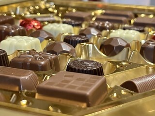 Chocolates of various shapes and flavors, in their golden colored box, with dark, milk, white and aluminum chocolate