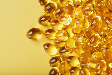 Pile of golden capsules of vitamin D3 on a yellow background with free space