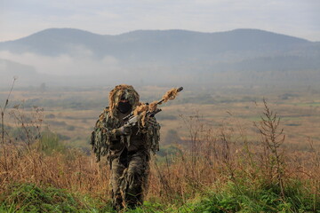 Sniper with Ghillies camouflage with sniper rifle with optics with empty landscape behind him, illustration photo for war