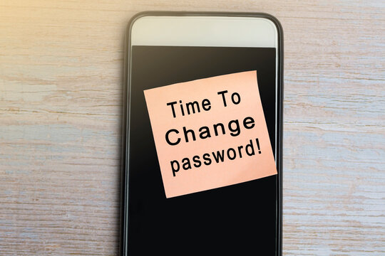 Time to change password text on notepad with smartphone on wooden desk.