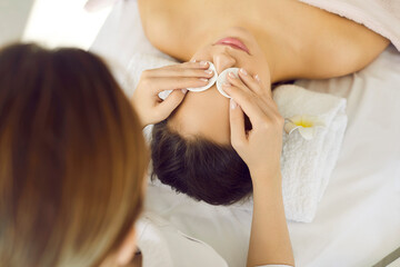 Obraz na płótnie Canvas Beautician at modern spa centre or beauty salon using cotton discs to remove makeup and clean skin on young woman's face before doing facial treatment like face massage, mask, or chemical exfoliation